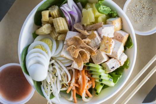 white bowl with tofu eggs corn onions bean sprouts carrots pineapple cucumber wonton strips with dressings on both sides