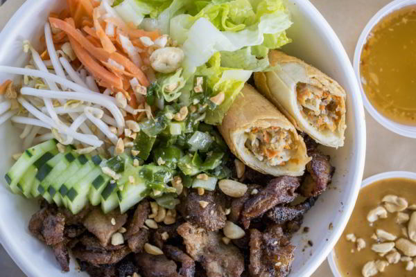 Bowl with bean sprouts beef cucumber carrots nuts spring cabbage and peanut sauce on the side